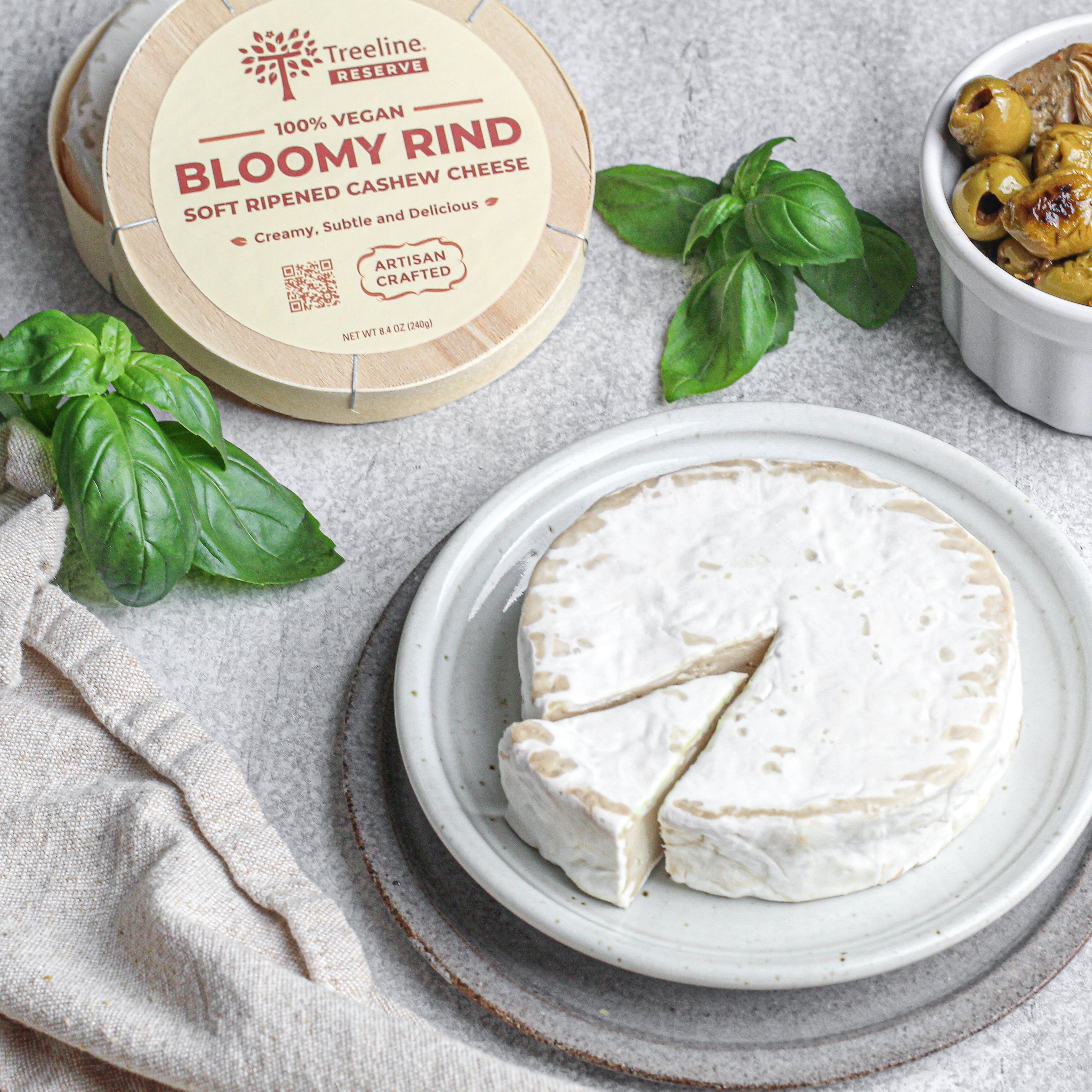 Wheel of bloomy rind on a plate with container and olives 